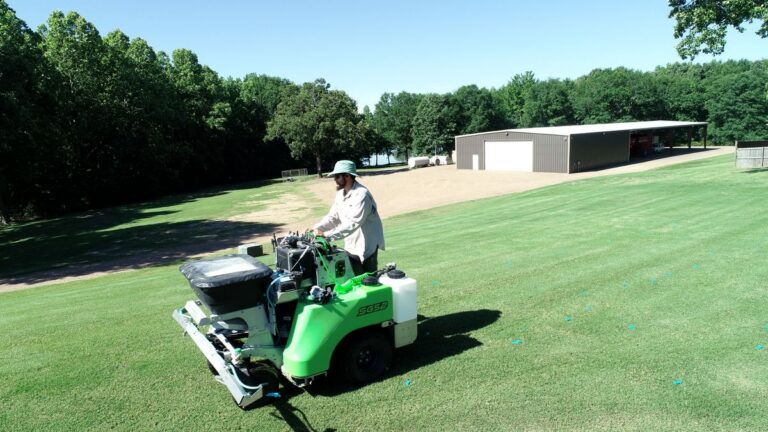 A uniformed Lawn Jox technician treating a bermuda lawn with a ride-on spray rig in north Mississippi