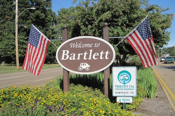 Welcome sign for Bartlett, TN, with American flags, vibrant landscaping, and Tree City USA recognition. Expert lawn care services available in Bartlett and surrounding Mid-South areas.