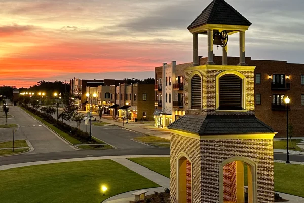 Scenic sunset view of Southaven, MS, featuring a well-lit bell tower, modern brick buildings, and a beautifully landscaped downtown area. A vibrant community with maintained green spaces and walkable streets.